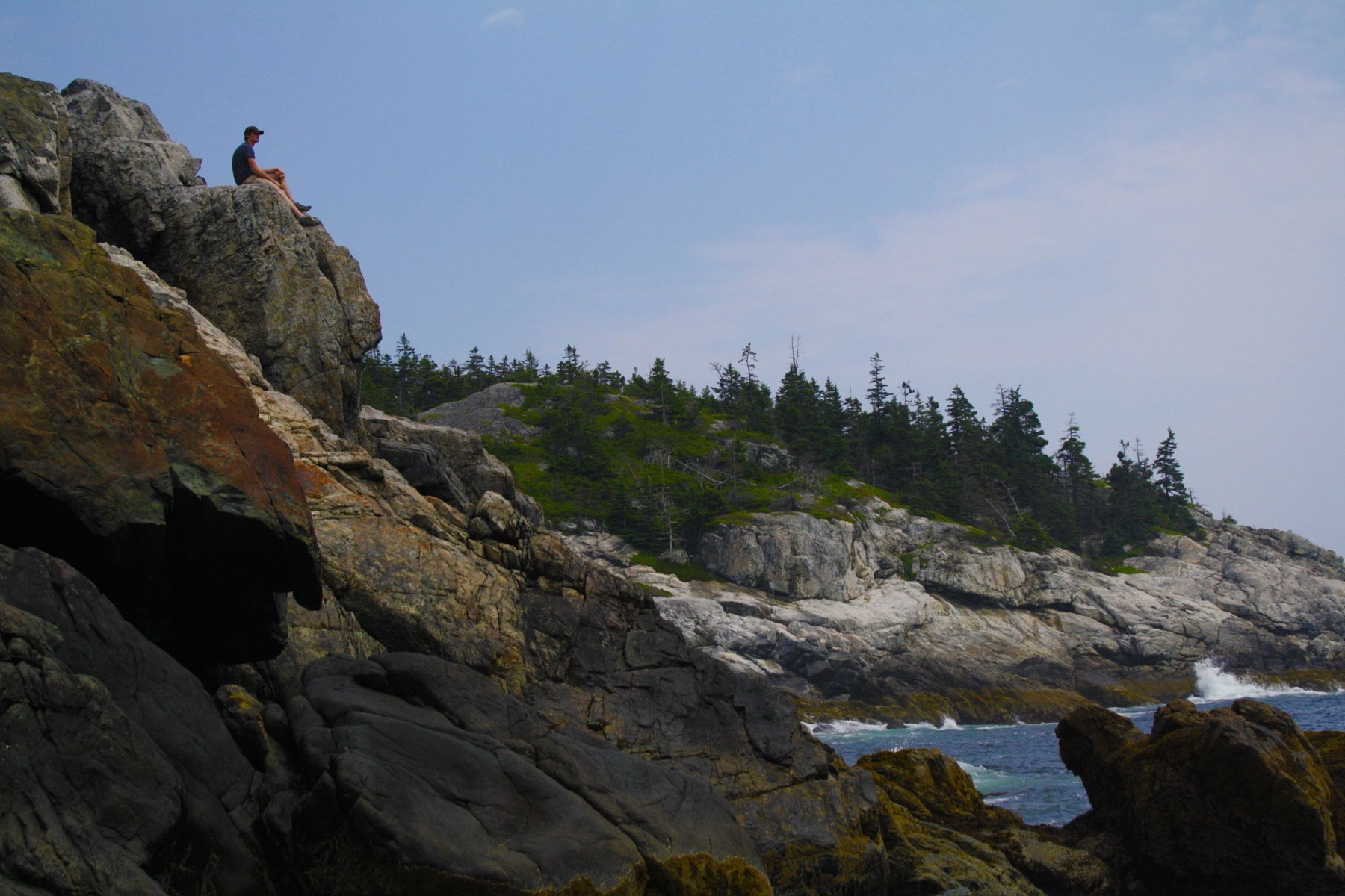 A figure resting on the rugged Maine coast